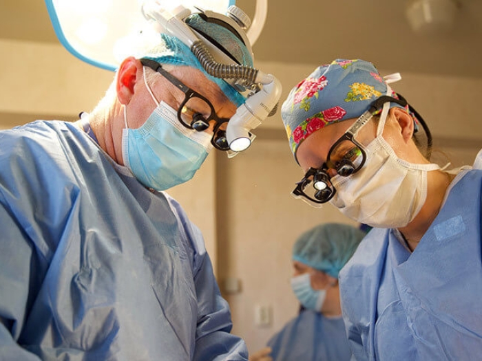 Surgeons wearing masks, gowns and glasses, light in background