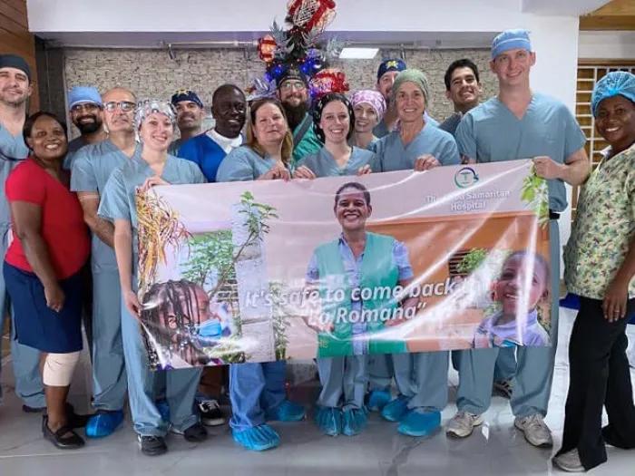 Surgery staff holding banner in hospital smiling wearing blue scrubs, It's safe to come back La Romana