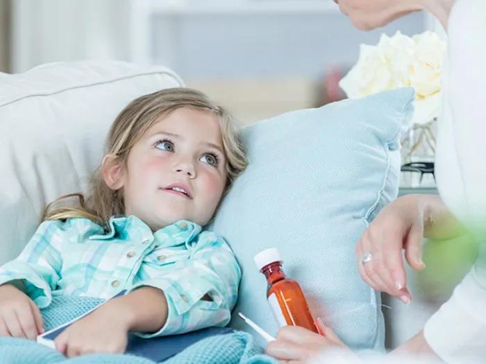 Little girl in bed with a woman next to her with a bottle of medicine in her hand
