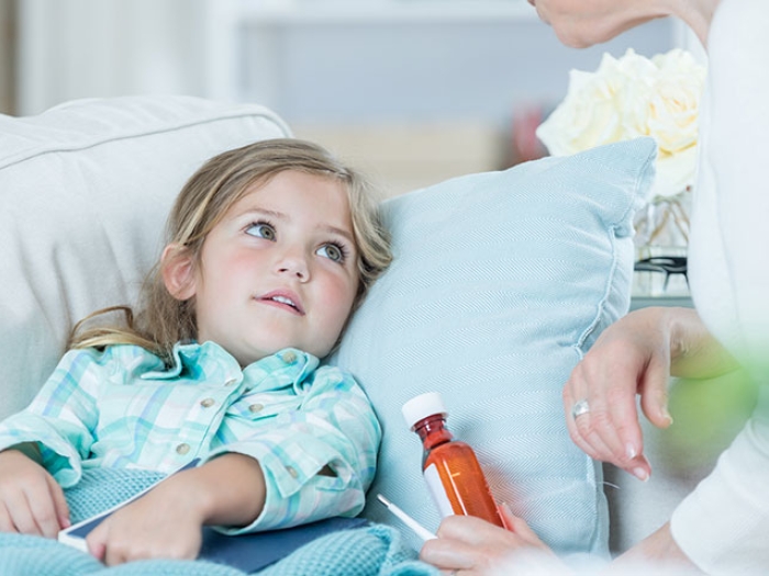 Little girl in bed with a woman next to her with a bottle of medicine in her hand