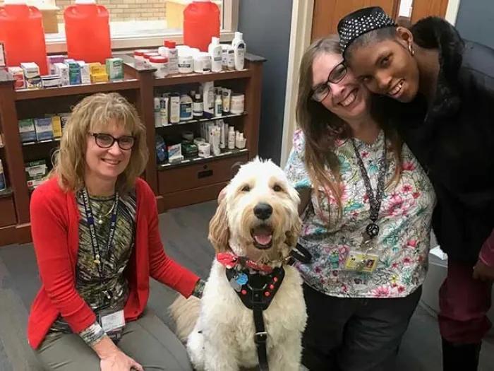 two women hugging dog and patient smiling for camera