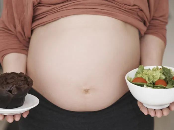 Pregnant woman with a salad in her left hand and a chocolate muffin in the left.