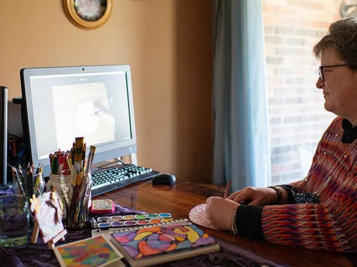 Woman artist watching a video and painting at table.