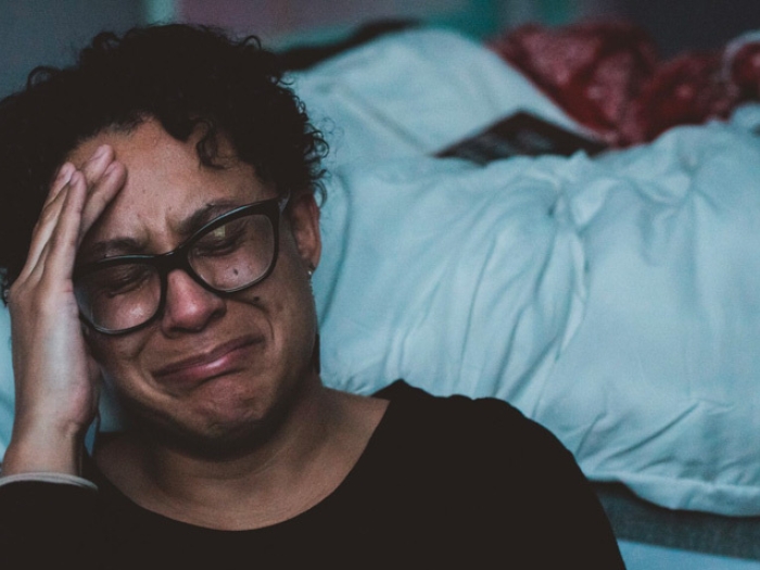 woman crying with glasses next to bed with white blanket 