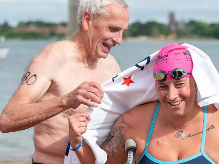 father drying off daughter on head with white towel with daughter wearing swim cap and goggles.