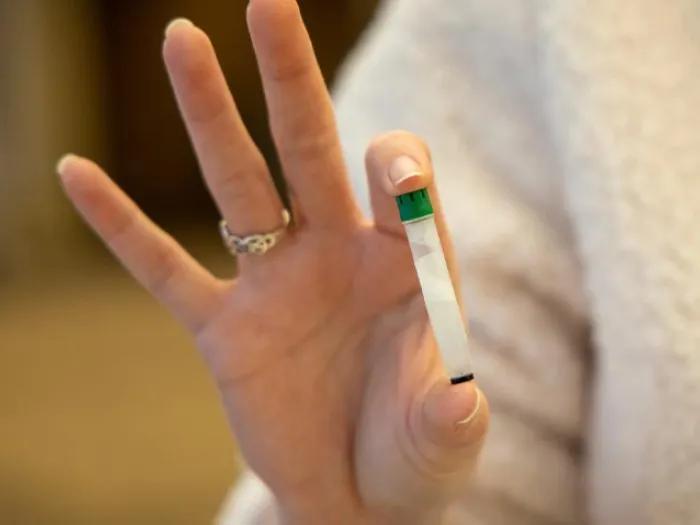 woman holding clear vial with green lid in two fingers