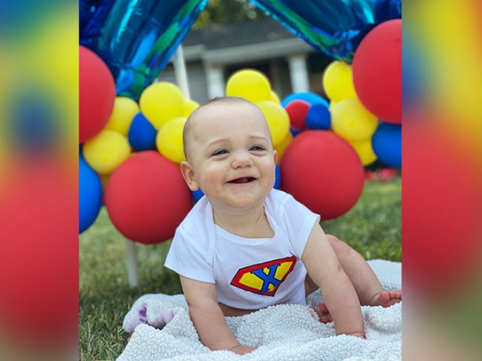 baby on law with red yellow and blue balloons in background