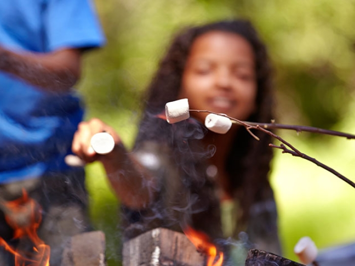 child holding stick of marshmallows over camp fire
