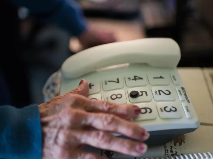 An elderly hand reaches for a large-button telephone.