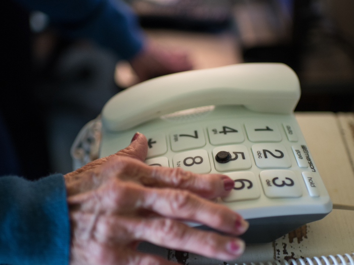 An elderly hand reaches for a large-button telephone.