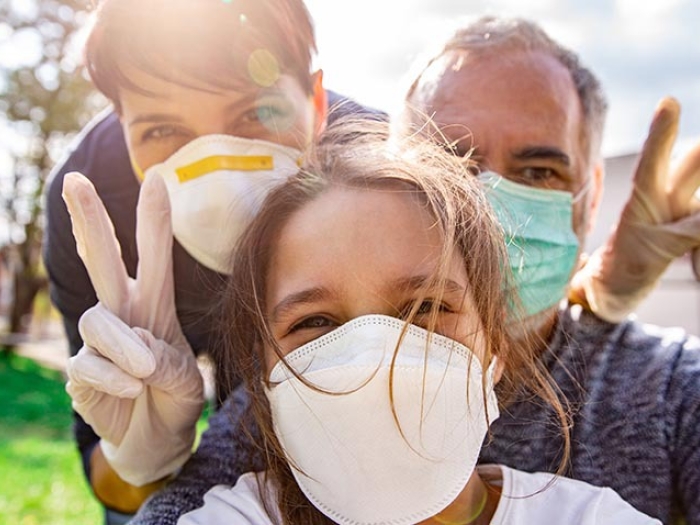 mom, dad and daughter taking selfie outside with peace signs and masks on