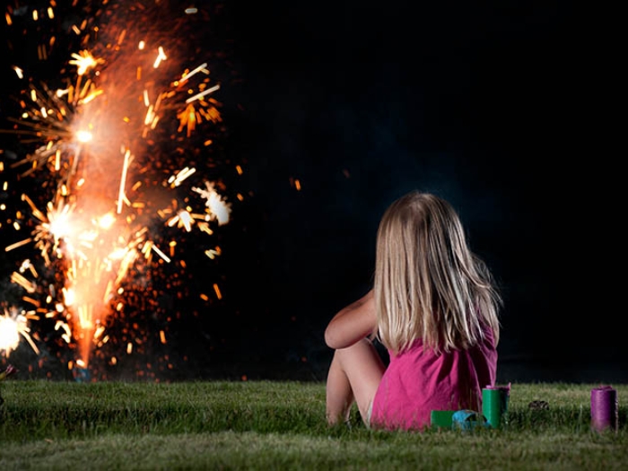 little girl sitting on grass watching fireworks
