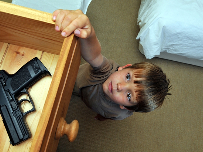 Child reaching for a gun laying in an open drawer