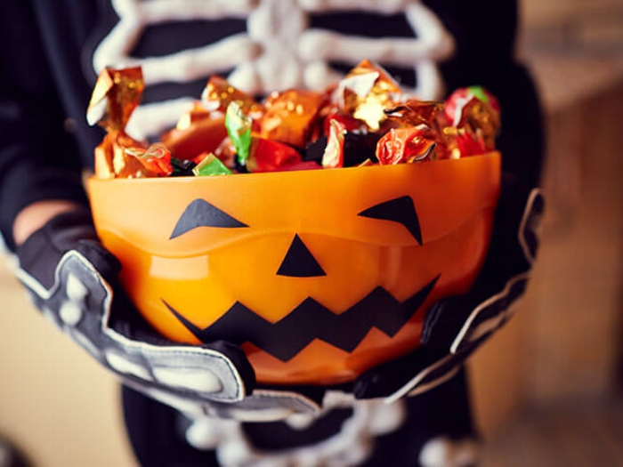 Kid holding pumpkin bowl of candy in skeleton costume