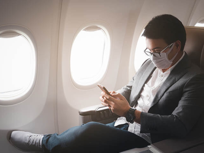 Male on airplane with mask using phone