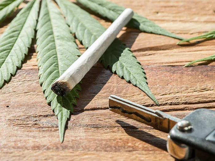 Car key and a marijuana cigarette laying on cannabis leaves