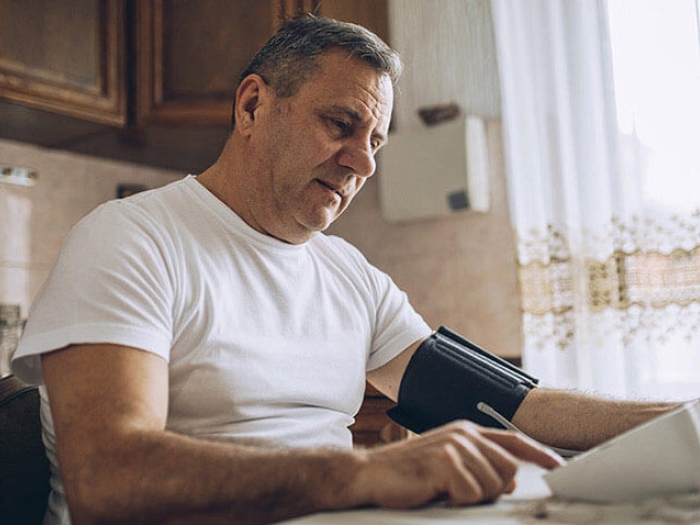 Older man looking at paper in kitchen while checking blood pressure