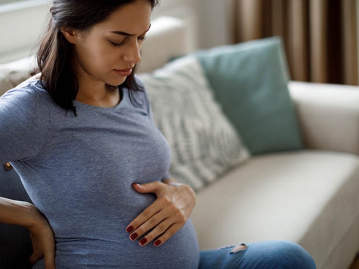pregnant woman holding stomach on couch in pain