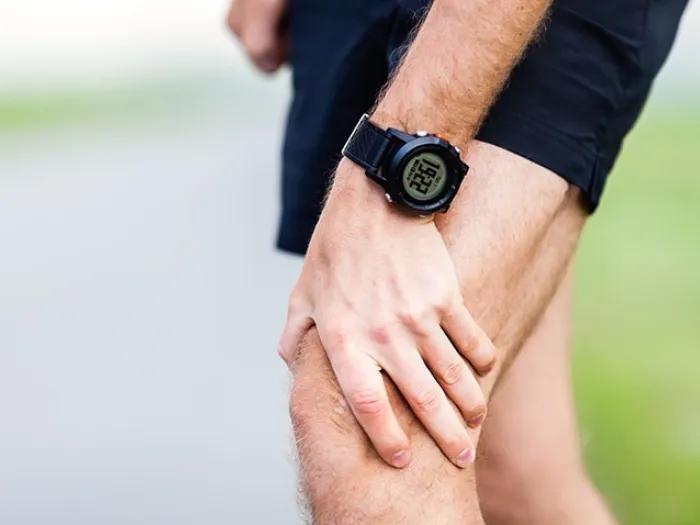 A person wearing a black digital watch holds their knee