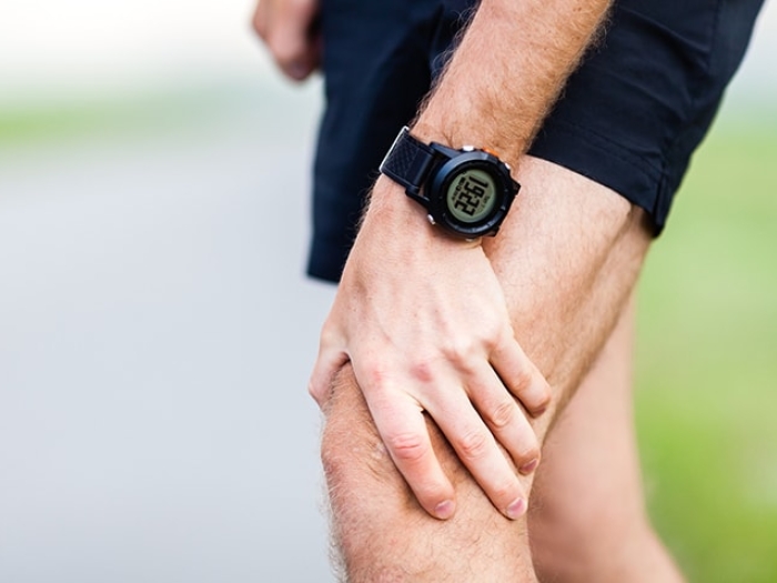 A person wearing a black digital watch holds their knee