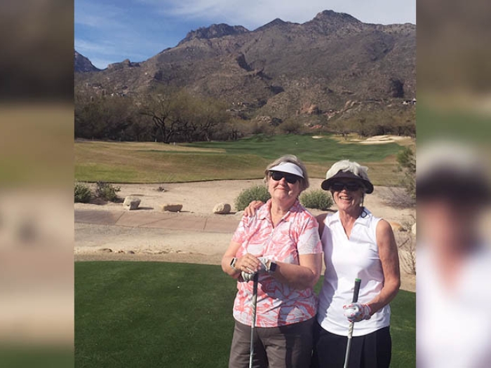 two ladies golfing in front of a mountain wearing hats
