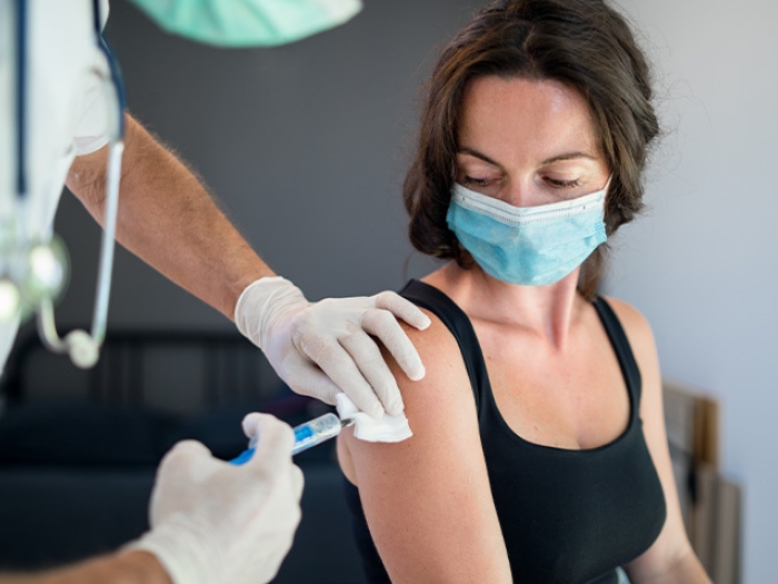 white woman getting vavvine in arm with mask on from practitioner with white gloves and stethoscope