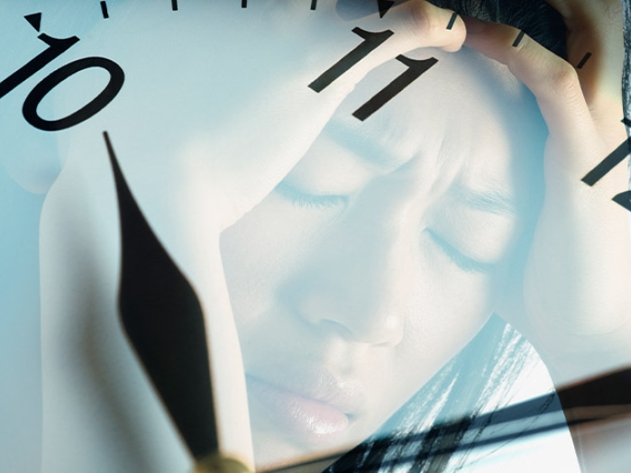 woman reflected in clock holding head in pain