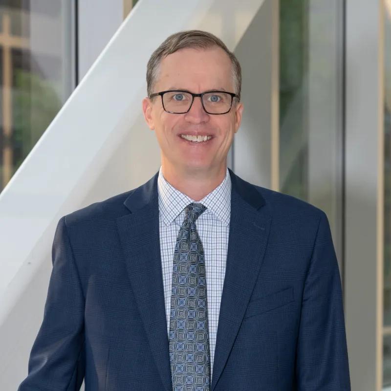 Portrait of David Miller, president of University of Michigan Health, wearing glasses, blue shirt and tie