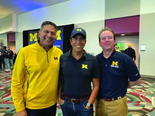 Three men are smiling at the camera. They're all wearing maize and blue.