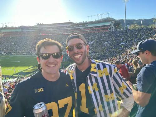Selfie of two people at a Michigan football game. They're both wearing sunglasses and maize and blue attire.