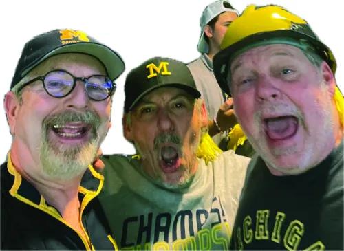 A selfie of three men wearing U of M gear and cheering. 