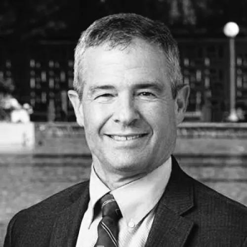Black and white headshot of Lawrence Shuer wearing a suit and tie. He's smiling and looking at the camera.