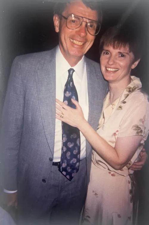 Lee Feldkamp and Rose O'Connor smiling and standing affectionately together. Lee is wearing a blue suit and tie and Rose is wearing a light-colored patterned dress.