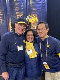 A photo of three adults, including U of M president Santa Ono, at a Michigan football tailgate.