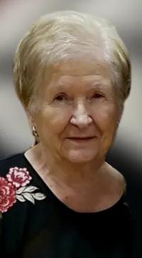 Portrait of Betty Dush. She has short gray hair, is smiling slightly, and is wearing a black top with pink roses on the shoulder.