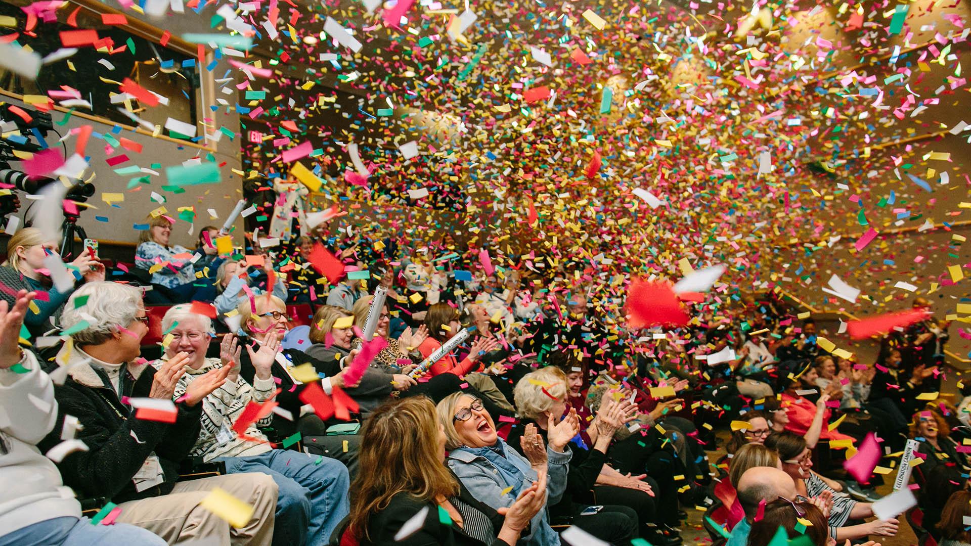 Joyful people clapping in an auditorium with colorful confetti filling the air