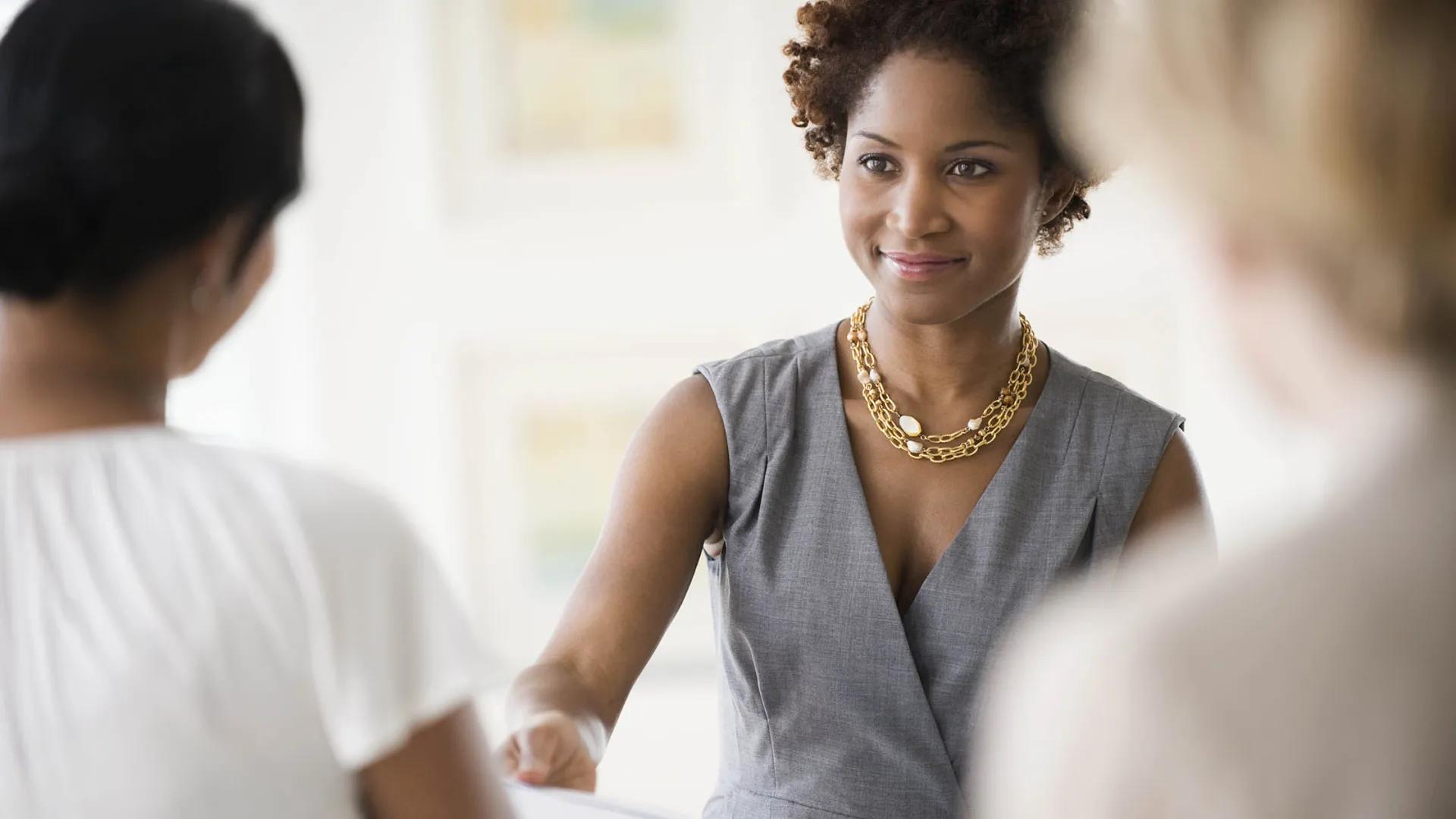 Professional young Black woman wearing dress handing papers to another woman