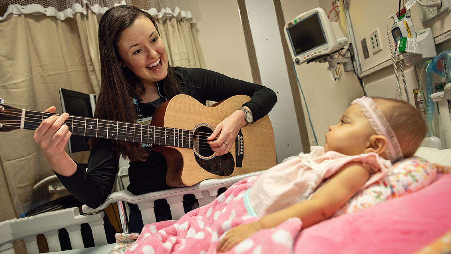 Woman smiling and a playing guitar to an infant patient