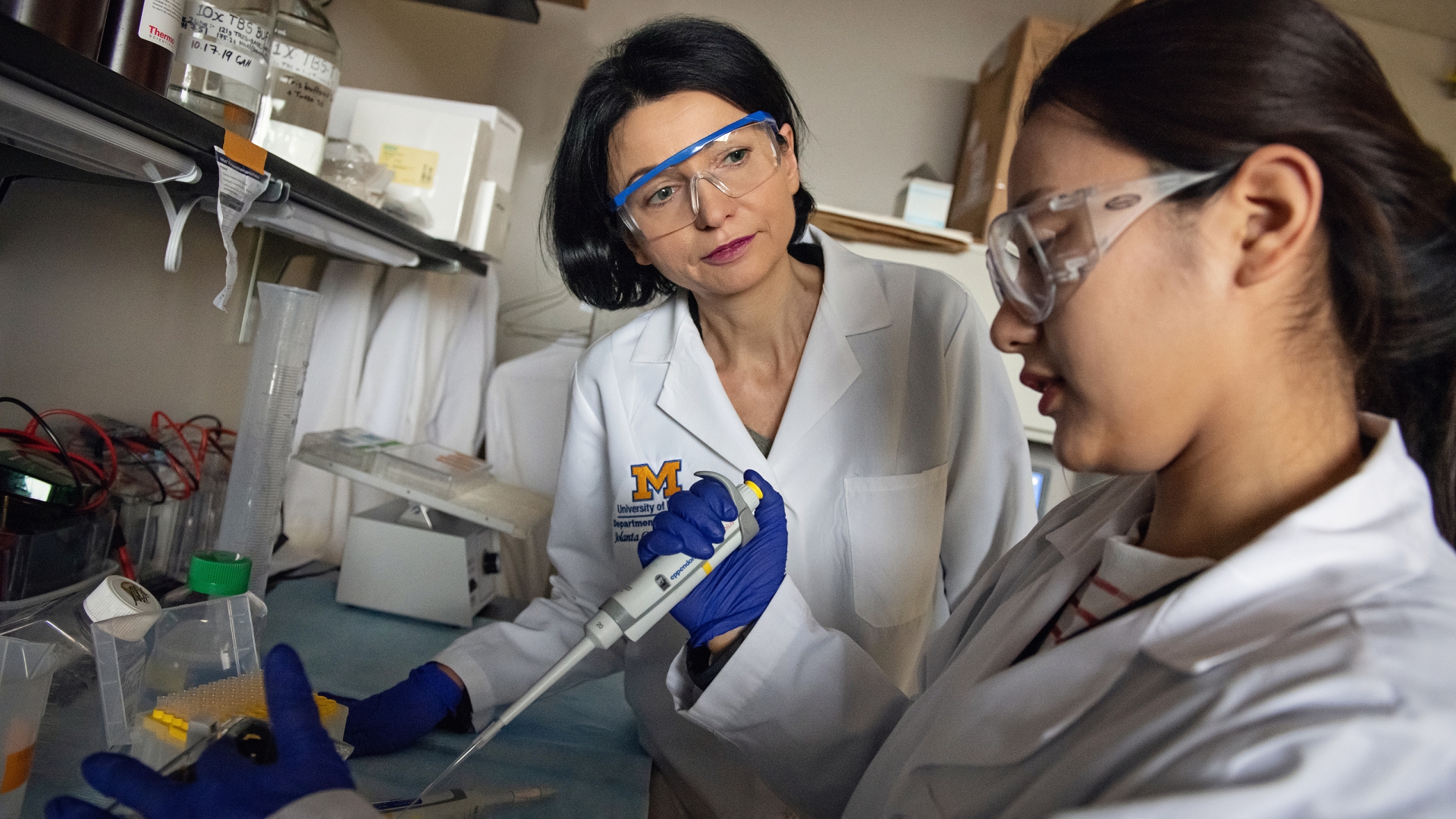 Two female researchers with black hair wearing goggles in research lab 