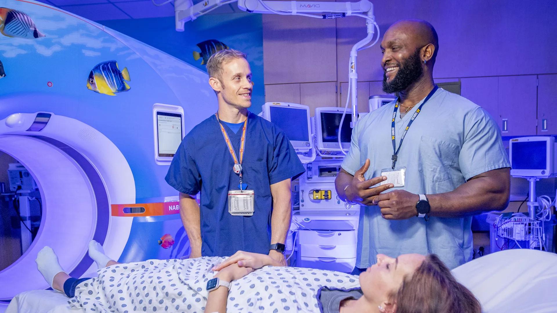 Two radiology techs in front of a CT scanner with a patient in the foreground