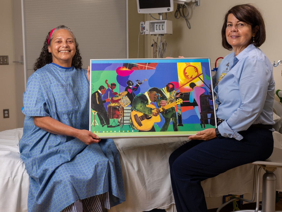Patient and female Gifts of Art staff member seated on bed displaying colorful art poster
