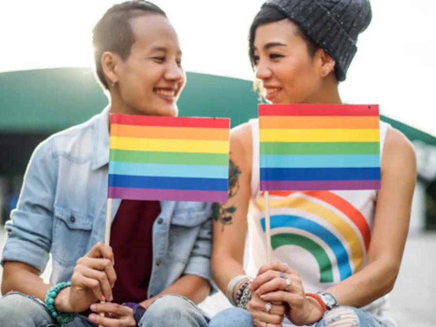 Two youth smile and hold pride flags
