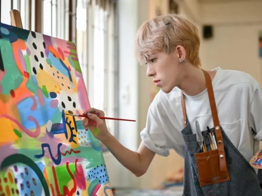 Person painting a colorful abstract canvas on an easel, holding a brush and palette.