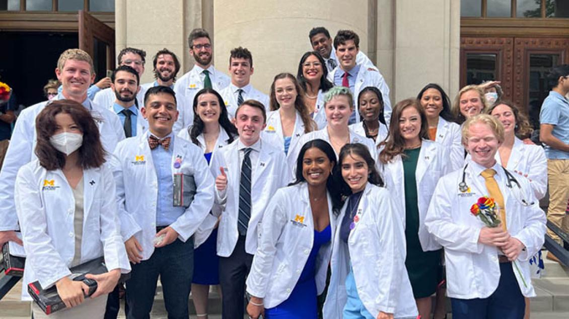 Group of medical students in white coats on steps of medical building, smiling 