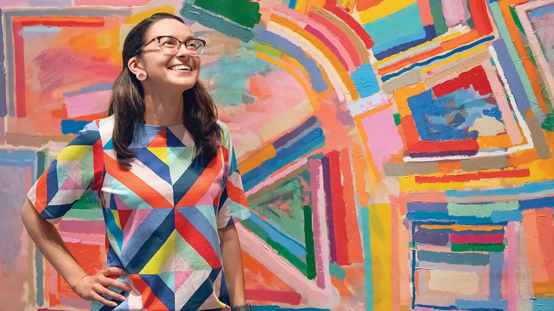 Emma smiles while standing in front of a colorful work of abstract art