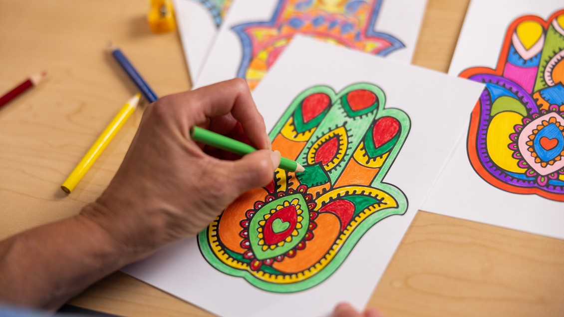 Hand holding green colored pencil coloring a Hamsa Hand project