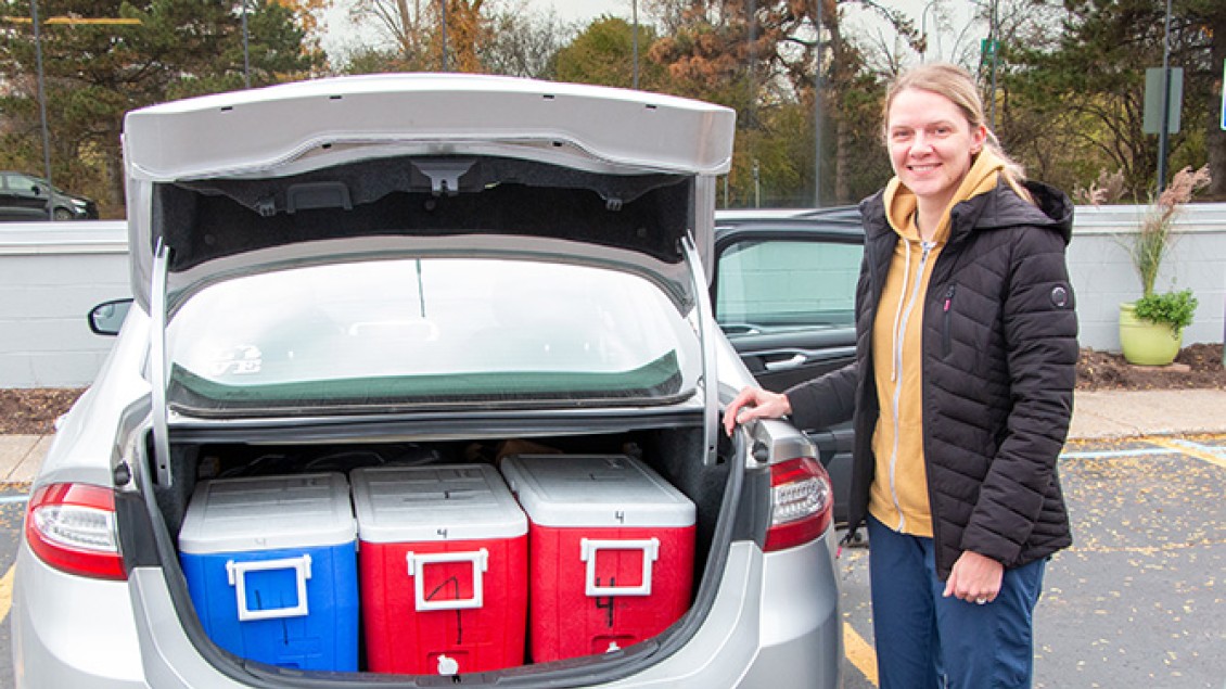 A volunteer smiles next to coolers in her vehicle's trunk