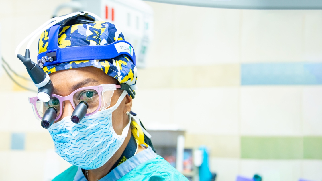 Female surgeon wearing a mask, loupes and a surgical cap with block Ms on it b
