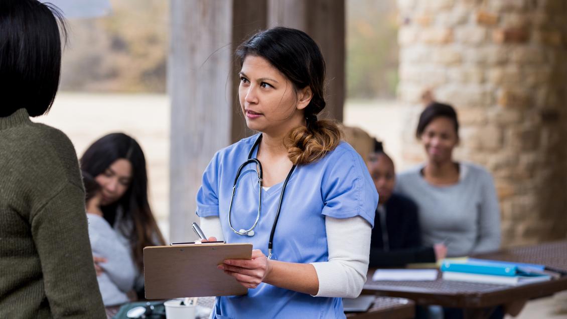 Female healthcare worker with stethoscope and clipboard talking to woman