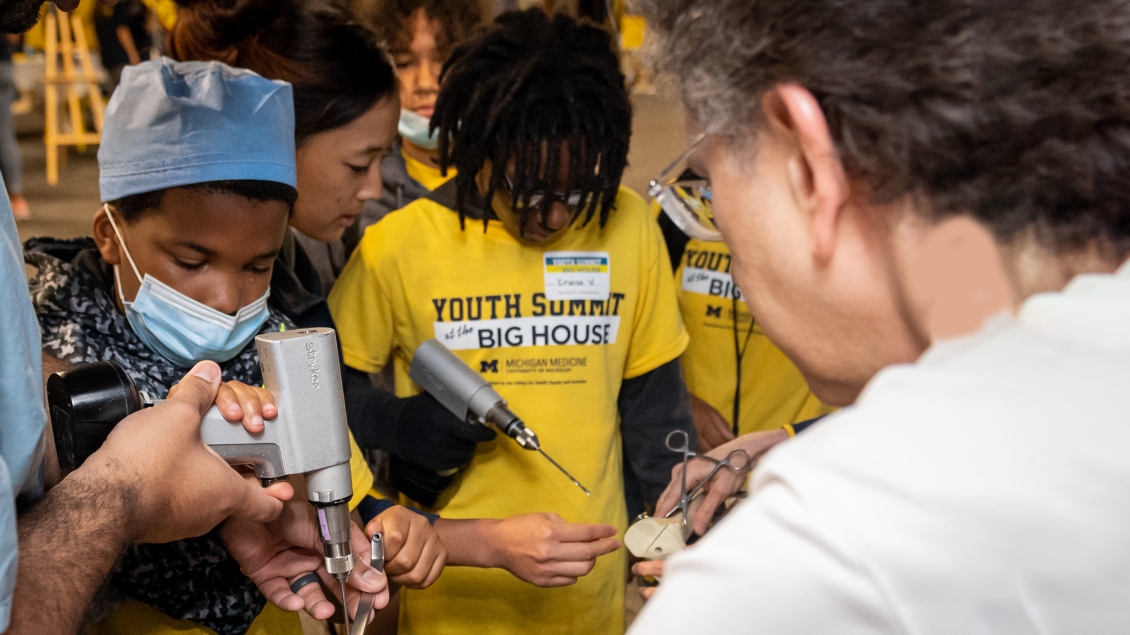 Young Black children wearing Youth Summit at the Big House tshirts with adults helping them to drill into bones